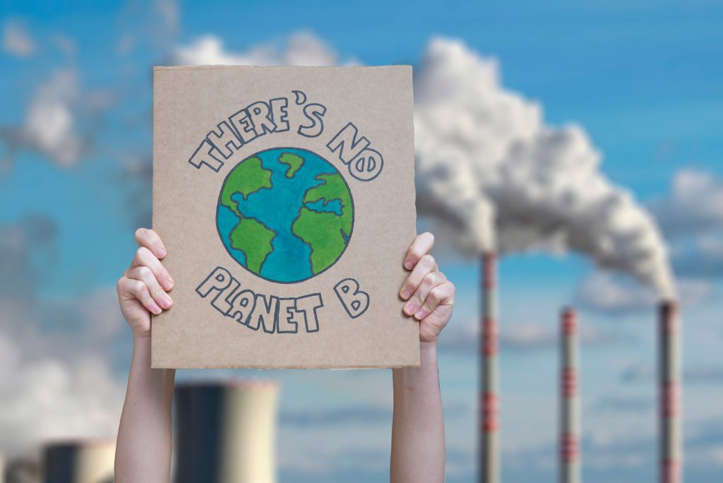 Pancarte écologique There's no planet B tenue devant des cheminées d'usine rejetant du CO2